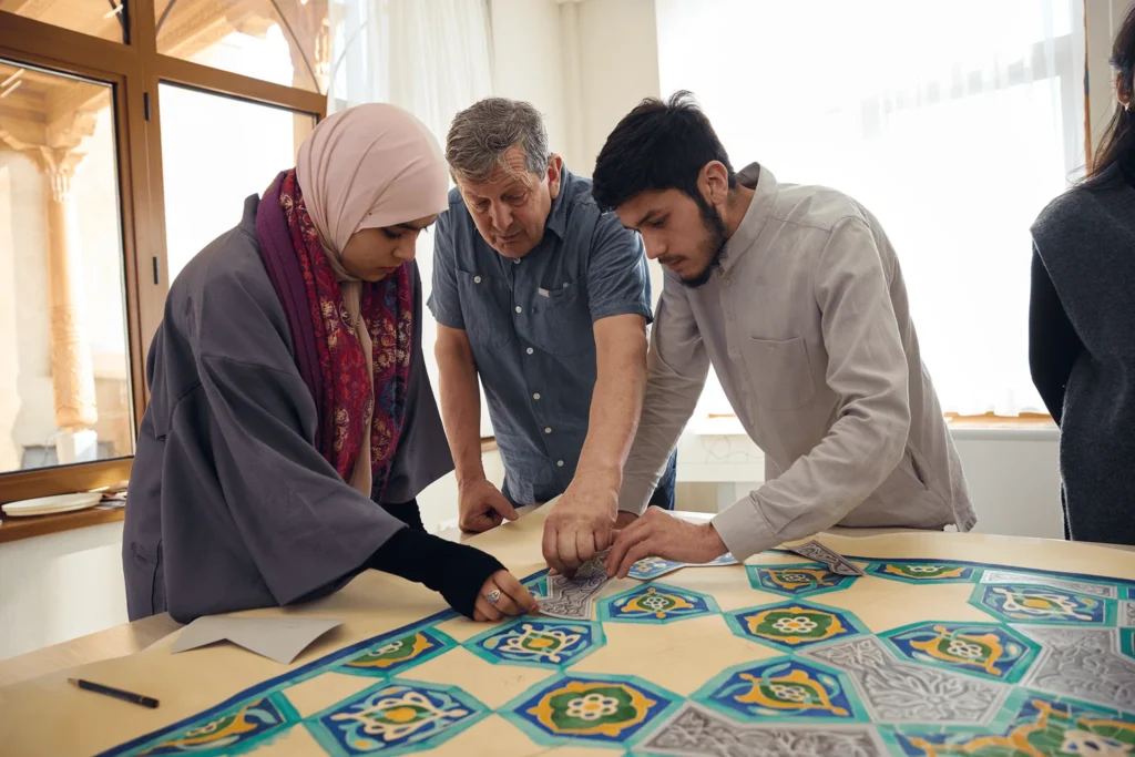 Отабек работает с преподавателем и другой студенткой над традиционным геометрическим узором.